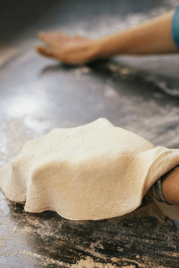 Person in Blue Shirt Holding a Pizza Dough